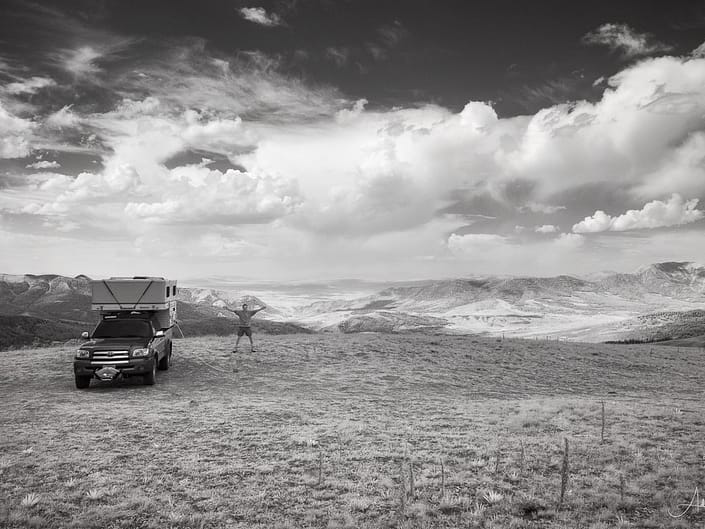 Photograph of man and camper parked at a spot in the Gravelly Range, Montant that overlooks adjacent mountains. Image was shot in infrared and converted to black and white.