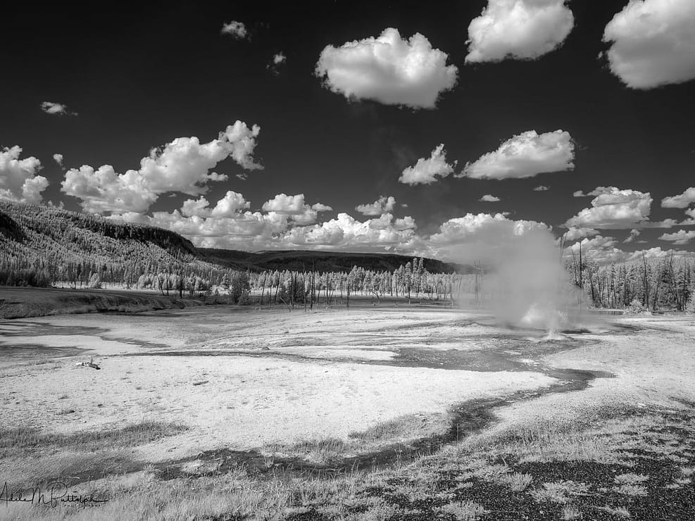 Black and white infrared photograph of erupting geysers and surrounding landscape. Shot in the Black Sand Geyser Basin, Yellowstone National Park, Wyoming.
